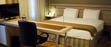 Una habitación de hotel con una cama, un escritorio con computadora, una silla y un televisor.