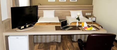 A hotel room with a bed, a desk with a TV, a laptop, a small fridge, and a chair.
