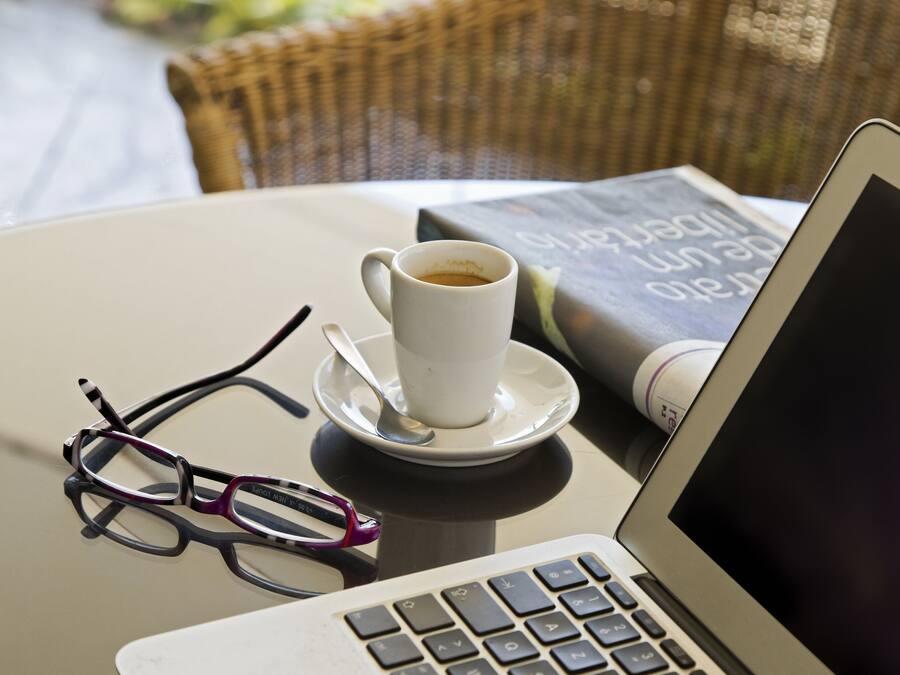 A laptop, a cup of coffee, a pair of glasses, and a book on a table.