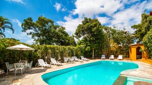 Una piscina con sillas de descanso y una mesa, rodeada de árboles y un cielo despejado.