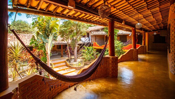 Un espacio al aire libre techado con una hamaca, paredes de ladrillo y vista a un edificio con techo de tejas.