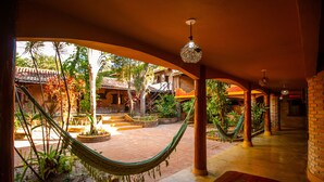 Un espacio al aire libre cubierto con una hamaca, columnas de ladrillo y vista a un edificio tradicional con tejado de tejas.