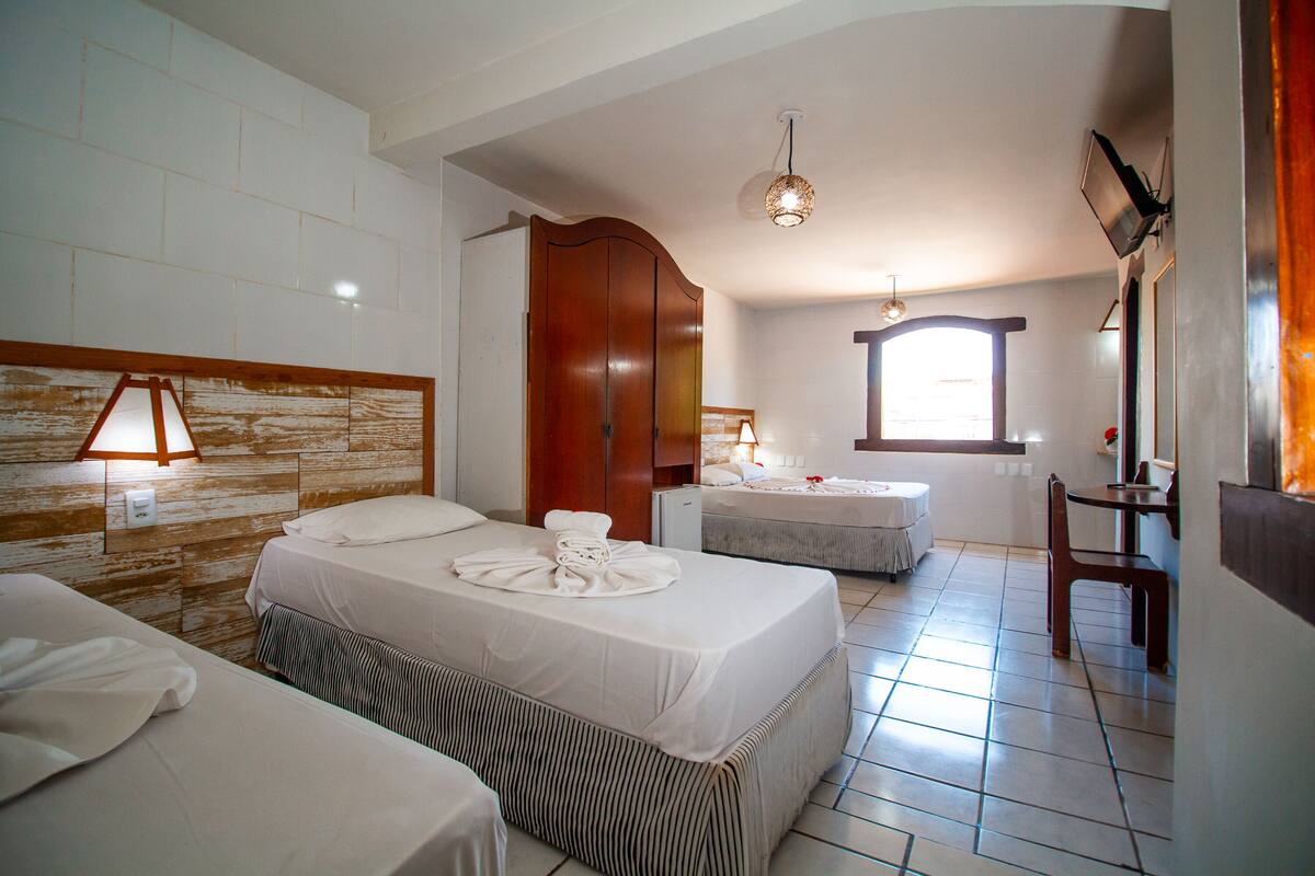 A hotel room with two beds, a desk, a chair, and a window.