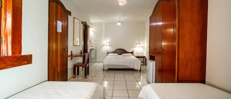 Quarto de hotel com duas camas, um guarda-roupa de madeira, uma escrivaninha e um espelho.