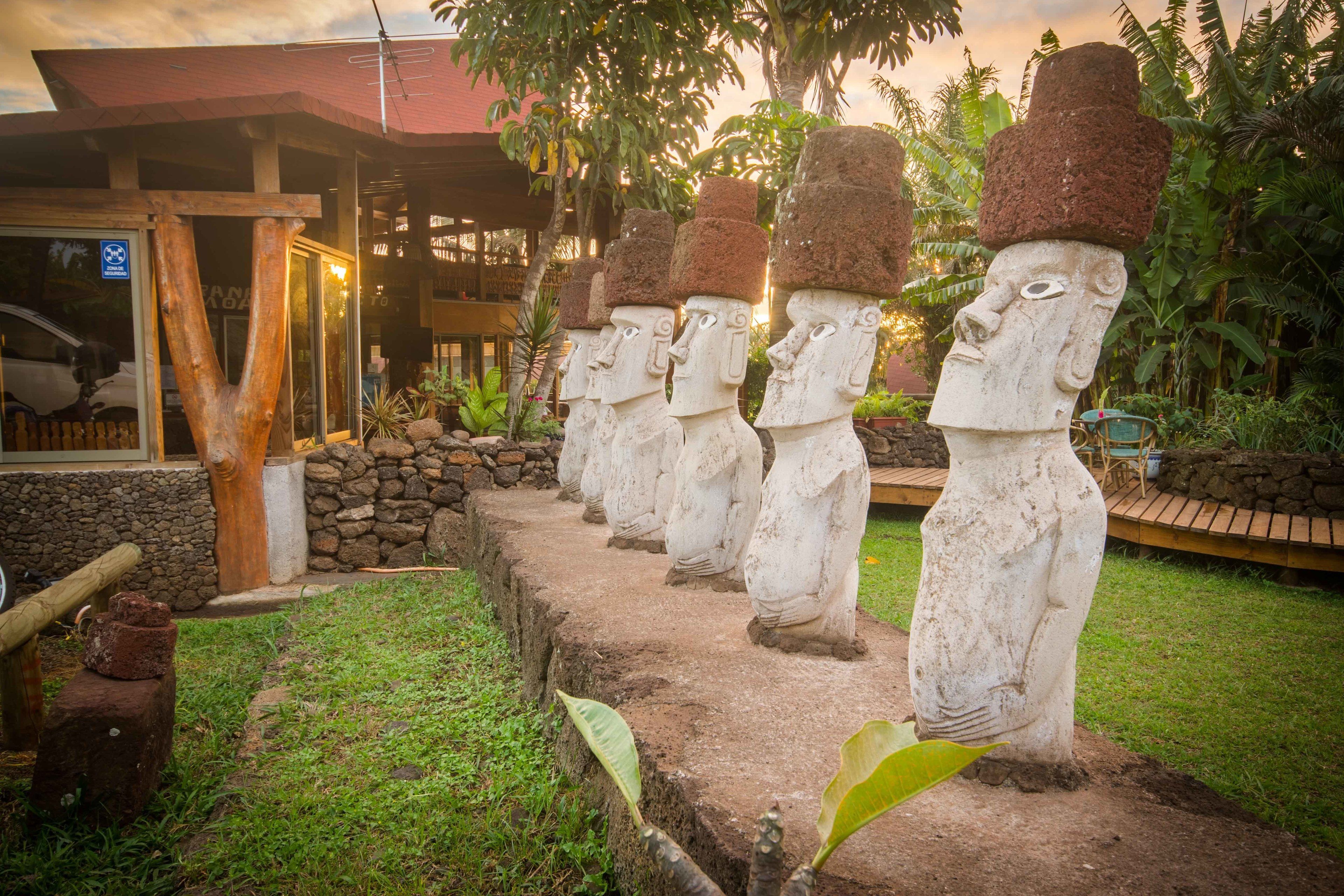 Una hilera de estatuas Moai en un jardín con un edificio al fondo.