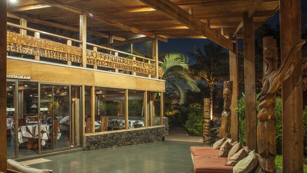 Un restaurante con fachada de vidrio, mesas al aire libre y decoración de madera.