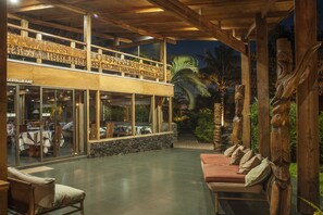Un restaurante con fachada de vidrio, mesas al aire libre y decoración de madera.