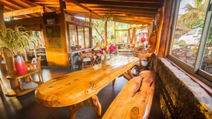 Un comedor de madera con bancos y una mesa larga, rodeado de sillas de madera y una planta en maceta.