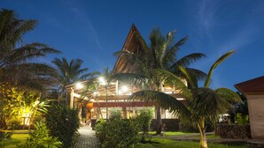Un hotel con un techo de forma piramidal destacada, rodeado de abundante vegetación y palmeras.