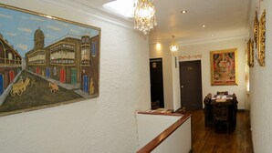 A hotel lobby with a reception desk, a chandelier, a painting of a building, and a door labeled 201. - Casa La Sambleña INN (Cusco)