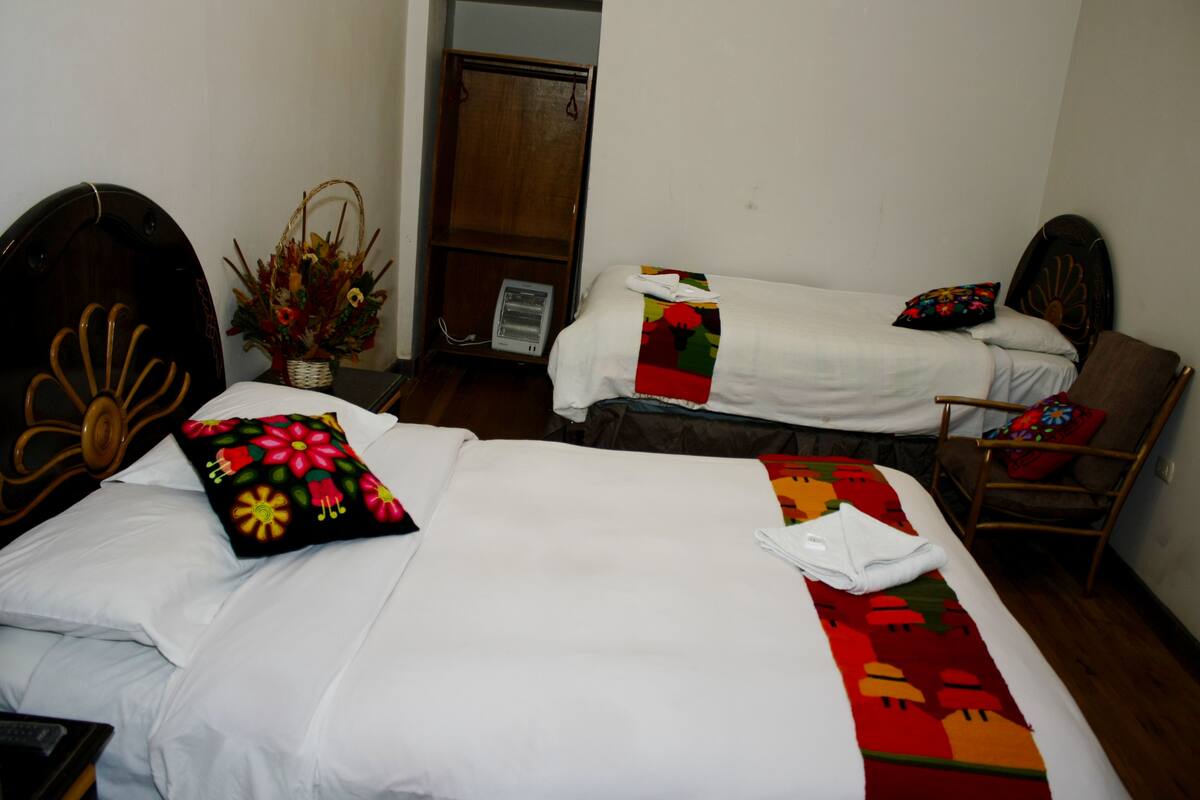 A hotel room with two beds, a wooden headboard, a chair, and a small table with a basket of flowers.
