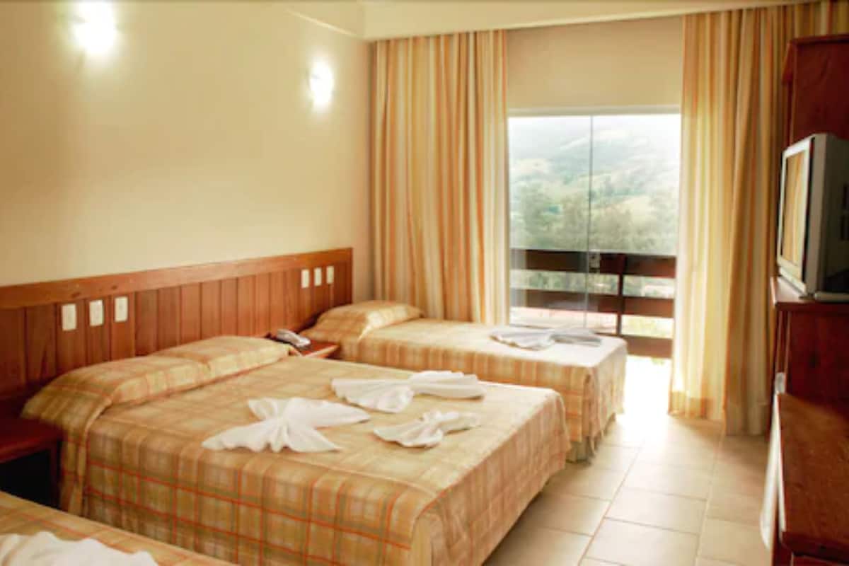 Habitación de hotel con dos camas, televisor y ventana con cortinas.