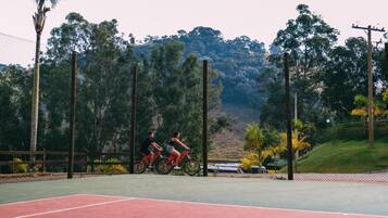 A tennis court with two cyclists riding on it.