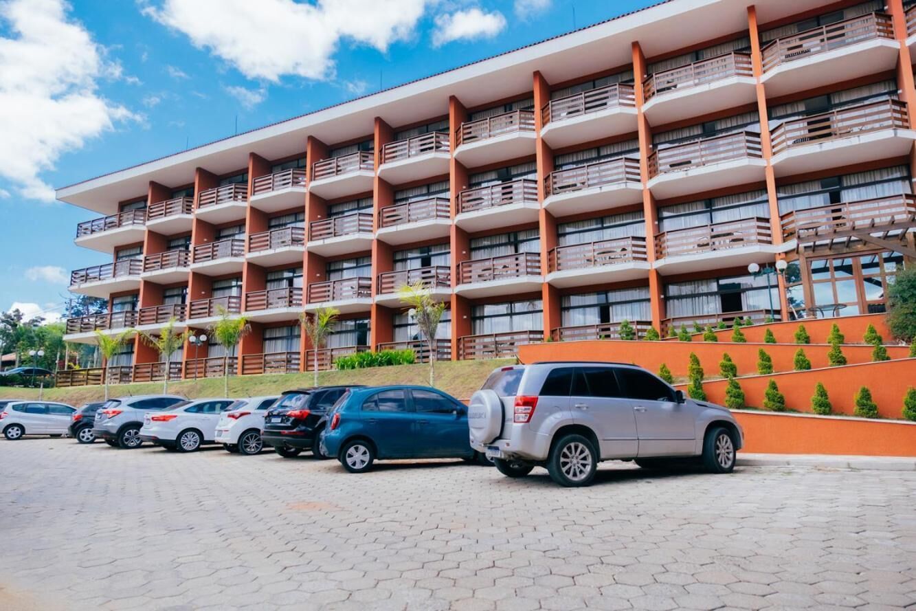 A multi-story hotel with balconies, a parking lot, and a landscaped area with small trees.