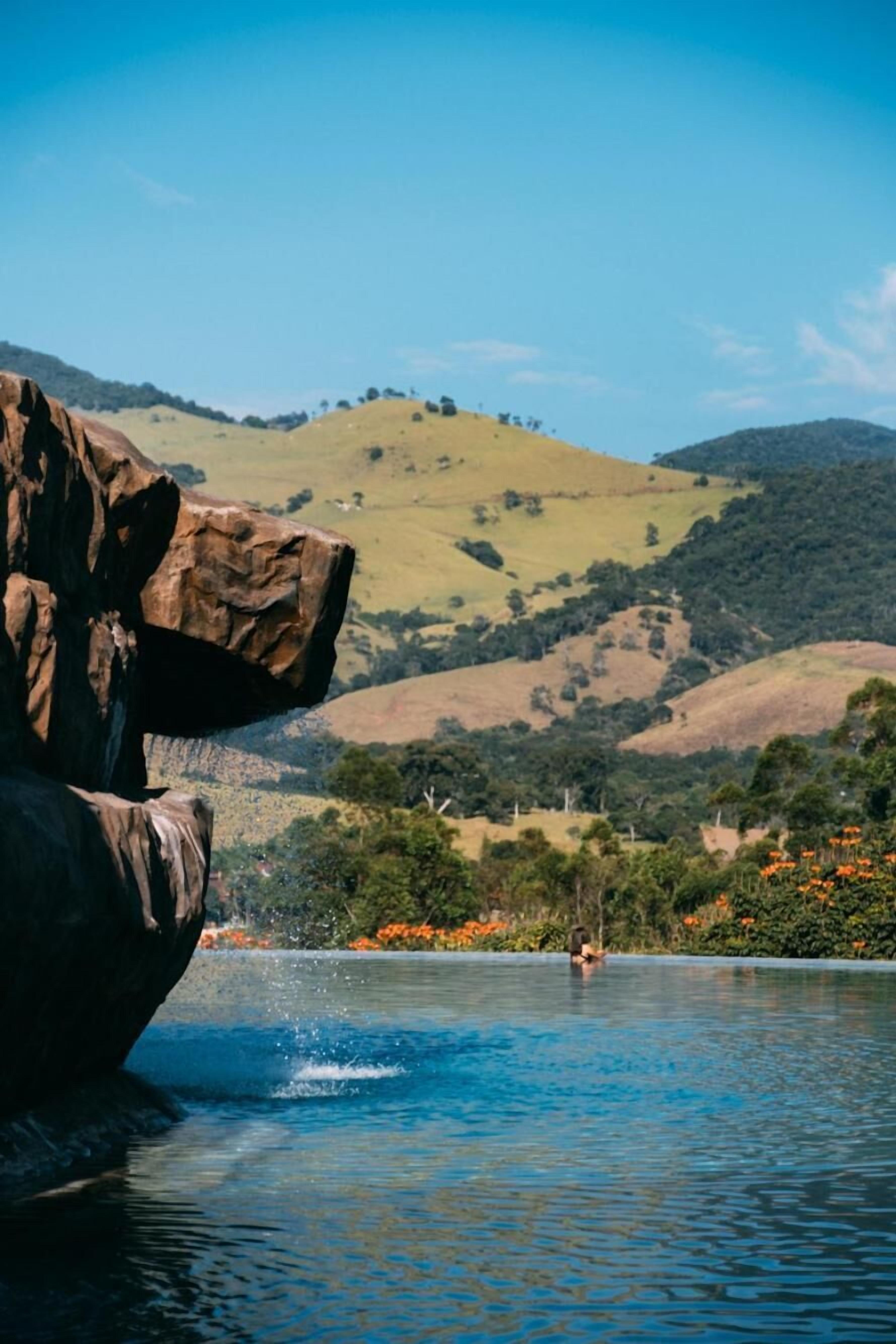 A natural landscape with a large rock formation, a body of water, and hills in the background.