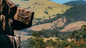 A natural landscape with a large rock formation, a body of water, and hills in the background.