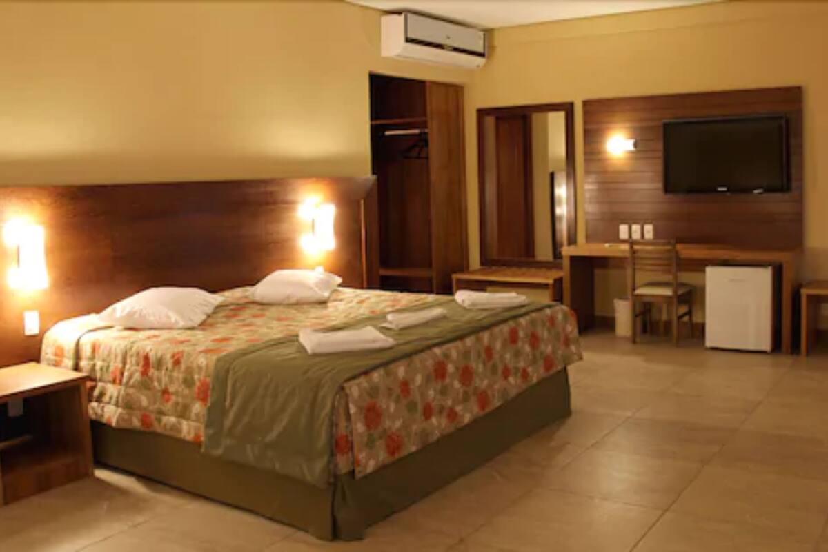 Habitación de hotel con cama, mesita de noche, escritorio con silla, televisor y armario.