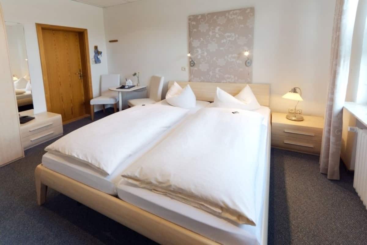 A hotel room with a double bed, a desk, a chair, a nightstand, and a lamp.