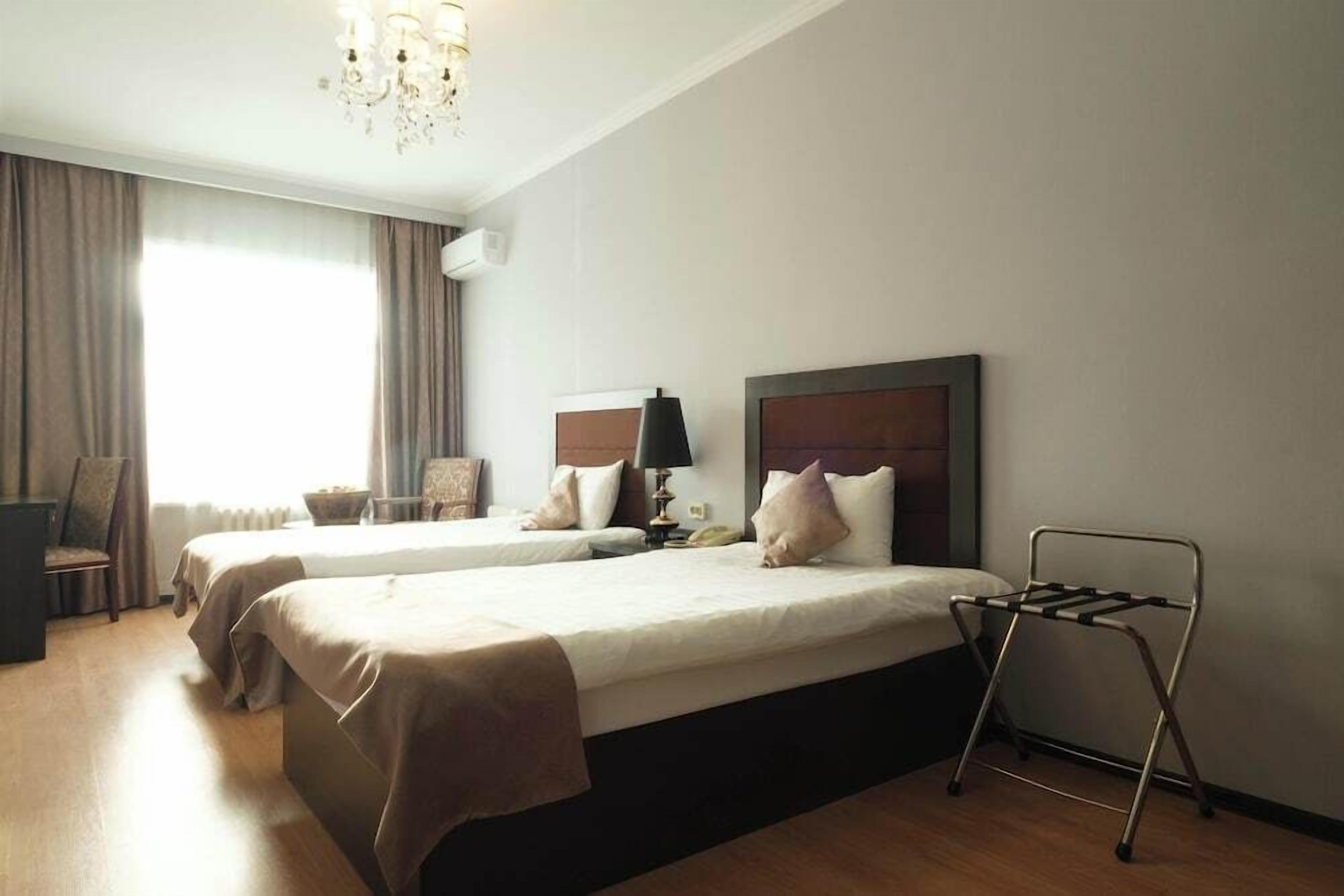A hotel room with two beds, a chair, a desk, and a chandelier.