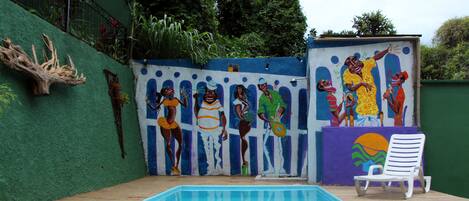 A swimming pool with a mural, a white chair, and a wooden deck.
