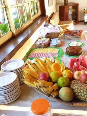 A buffet table with various fruits, pastries, and a stack of plates. - Pousada Portal de Paraty (Paraty)