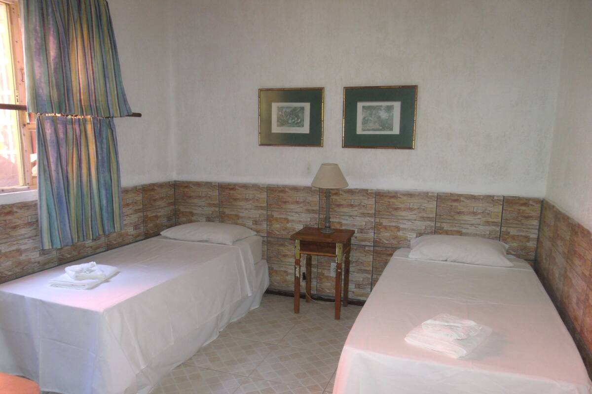 Une chambre d’hôtel avec deux lits simples, une petite table avec une lampe et deux tableaux encadrés au mur.