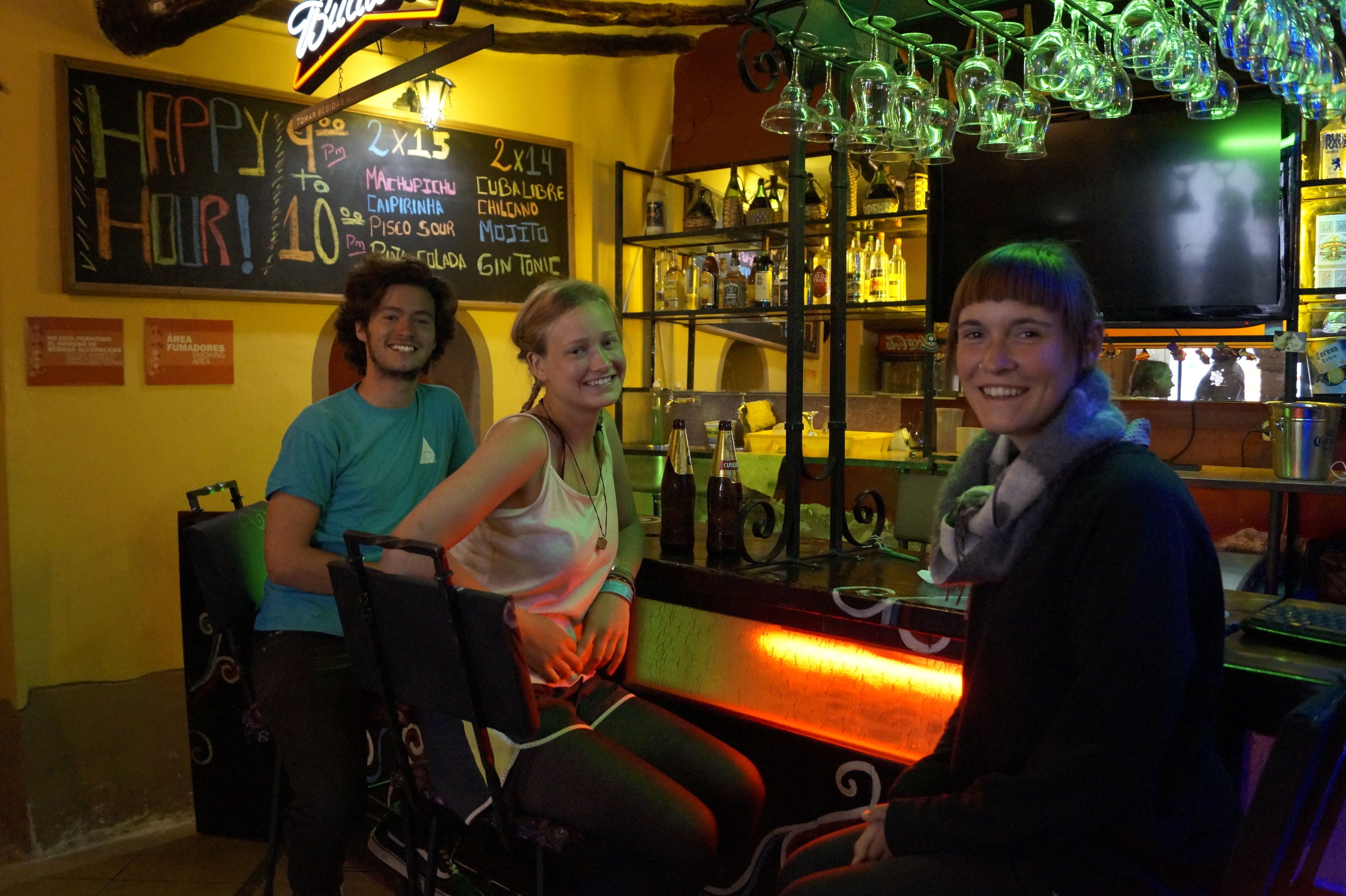A bar area with a chalkboard menu, shelves with bottles, and a neon sign.