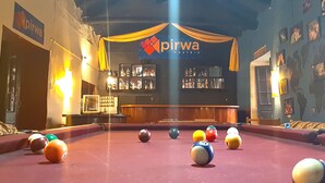 Une table de billard avec des billes, un coin bar avec un mini-bar, et une enseigne indiquant « auberges de jeunesse Pirwa ».