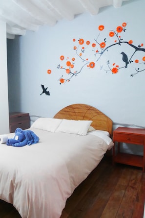 A bedroom with a bed, a nightstand, and a wall mural. - Pirwa Colonial Hostel (Cusco)