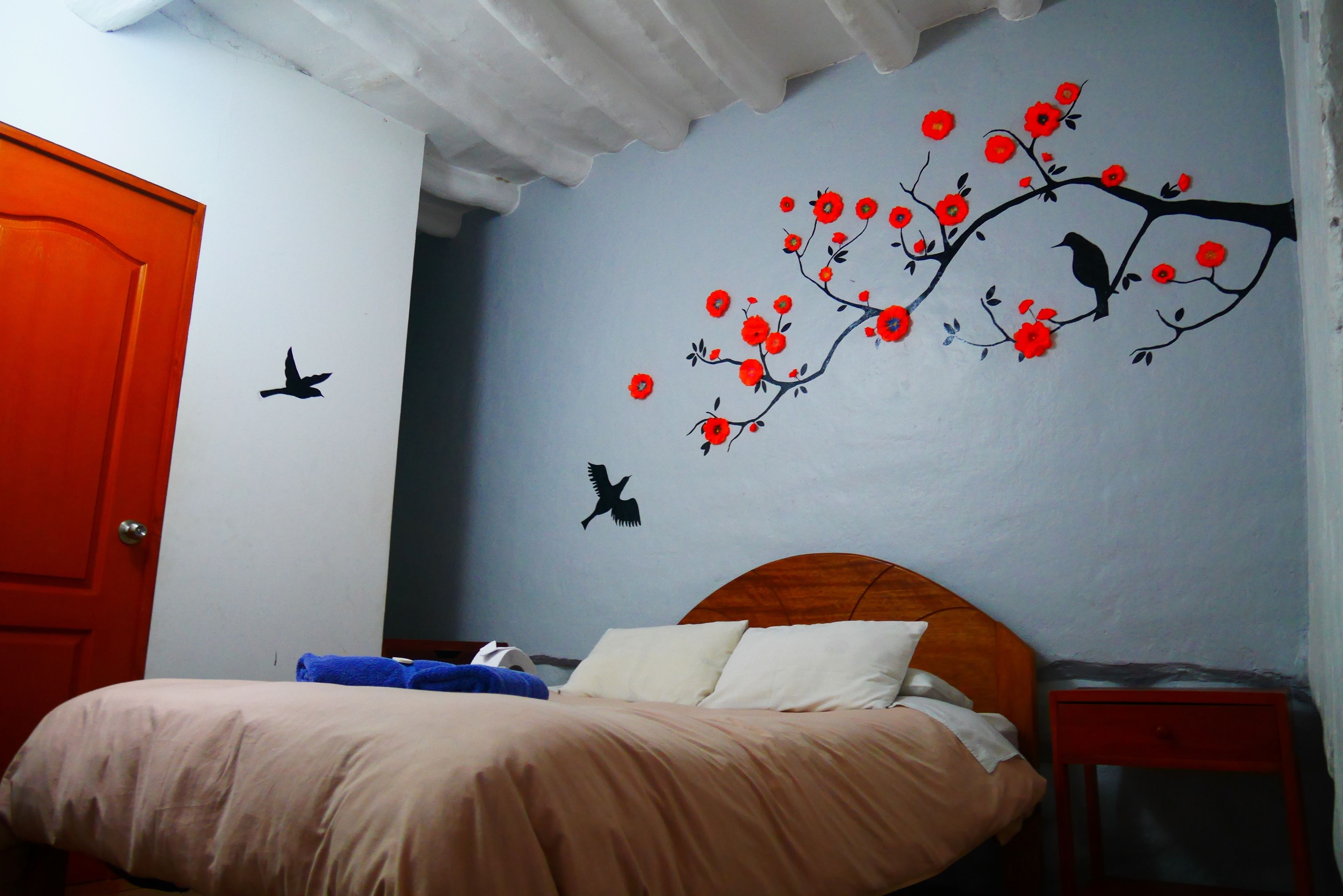 A bedroom with a bed, a wooden headboard, a nightstand, and a wall with a tree and bird decal.