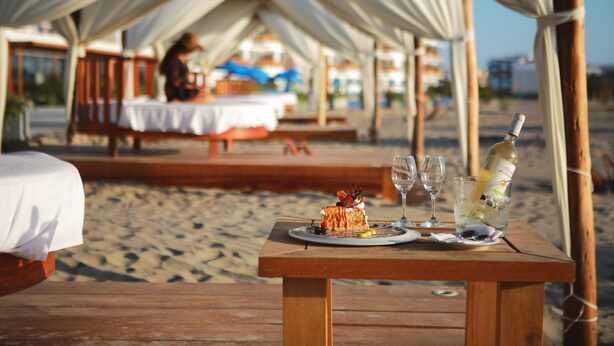 A wooden table with a dessert and drinks on a beach, under a tented area. - Hotel San Agustín Paracas (Paracas)
