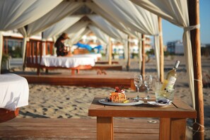 A wooden table with a dessert and drinks on a beach, under a tented area. - Hotel San Agustín Paracas (Paracas)