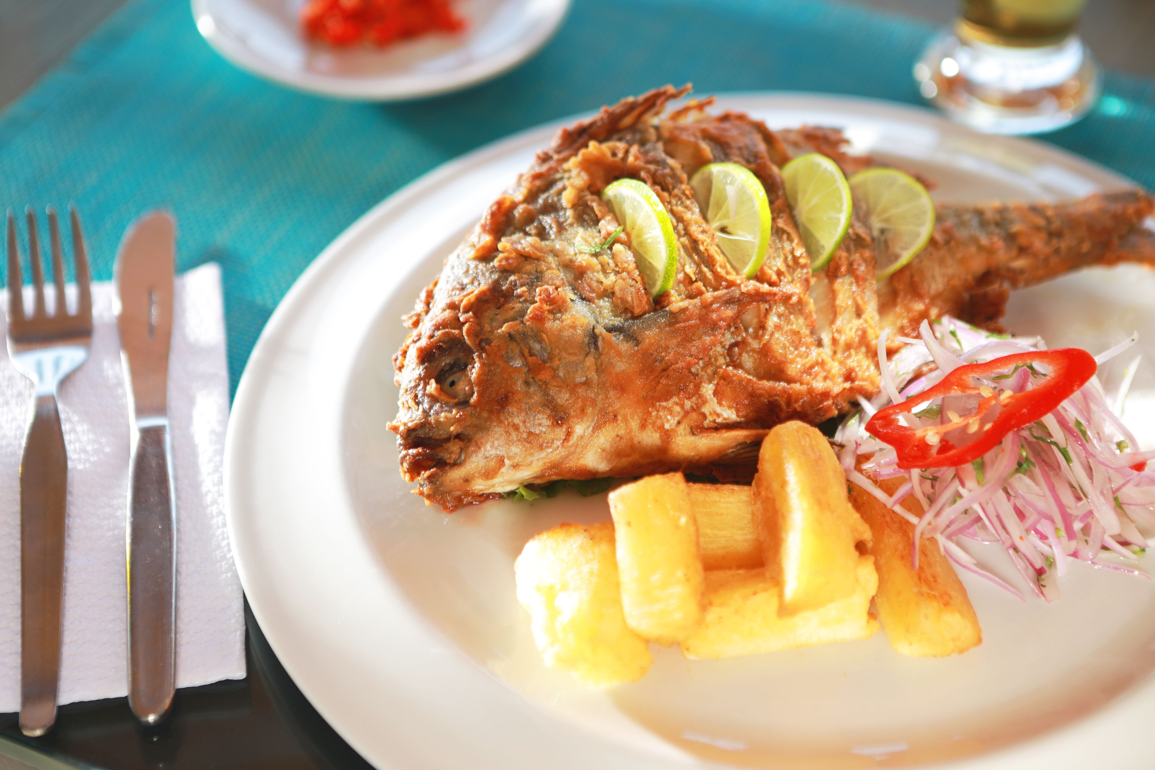 Un plato con pescado frito, gajos de lima y una porción de papas fritas.