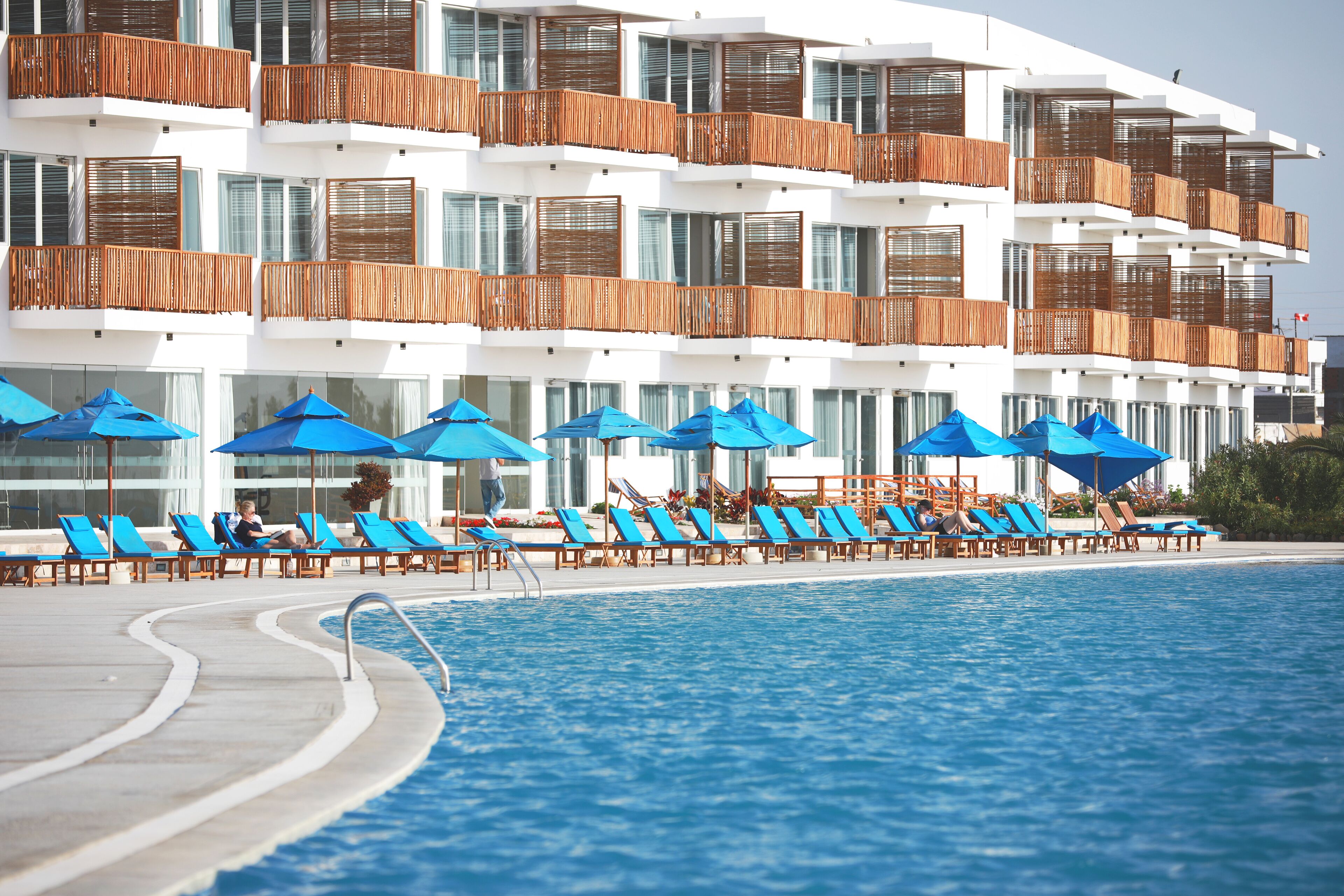Un hotel con zona de piscina, sombrillas azules y tumbonas.