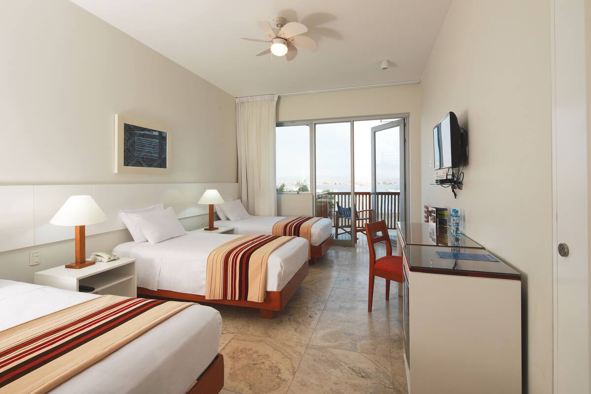 A hotel room with two beds, a desk, a chair, a television, and a balcony with a view.