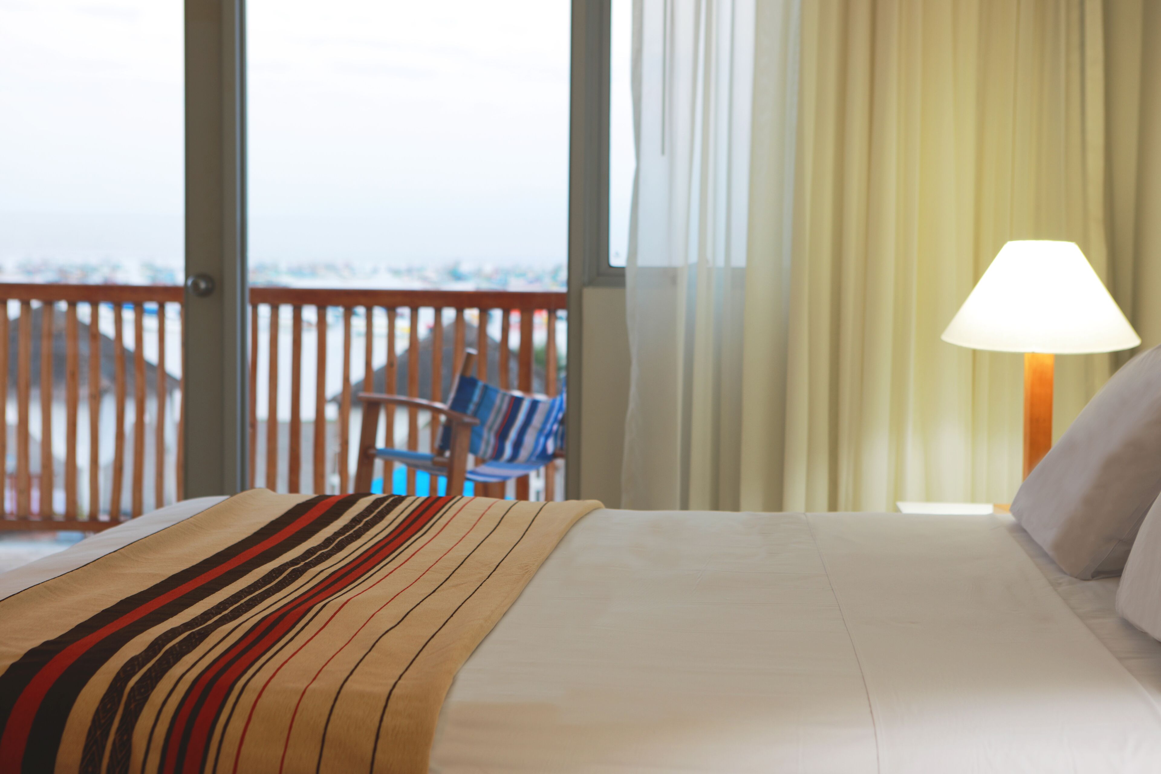 A hotel room with a bed, a chair, a lamp, and a view through the window.