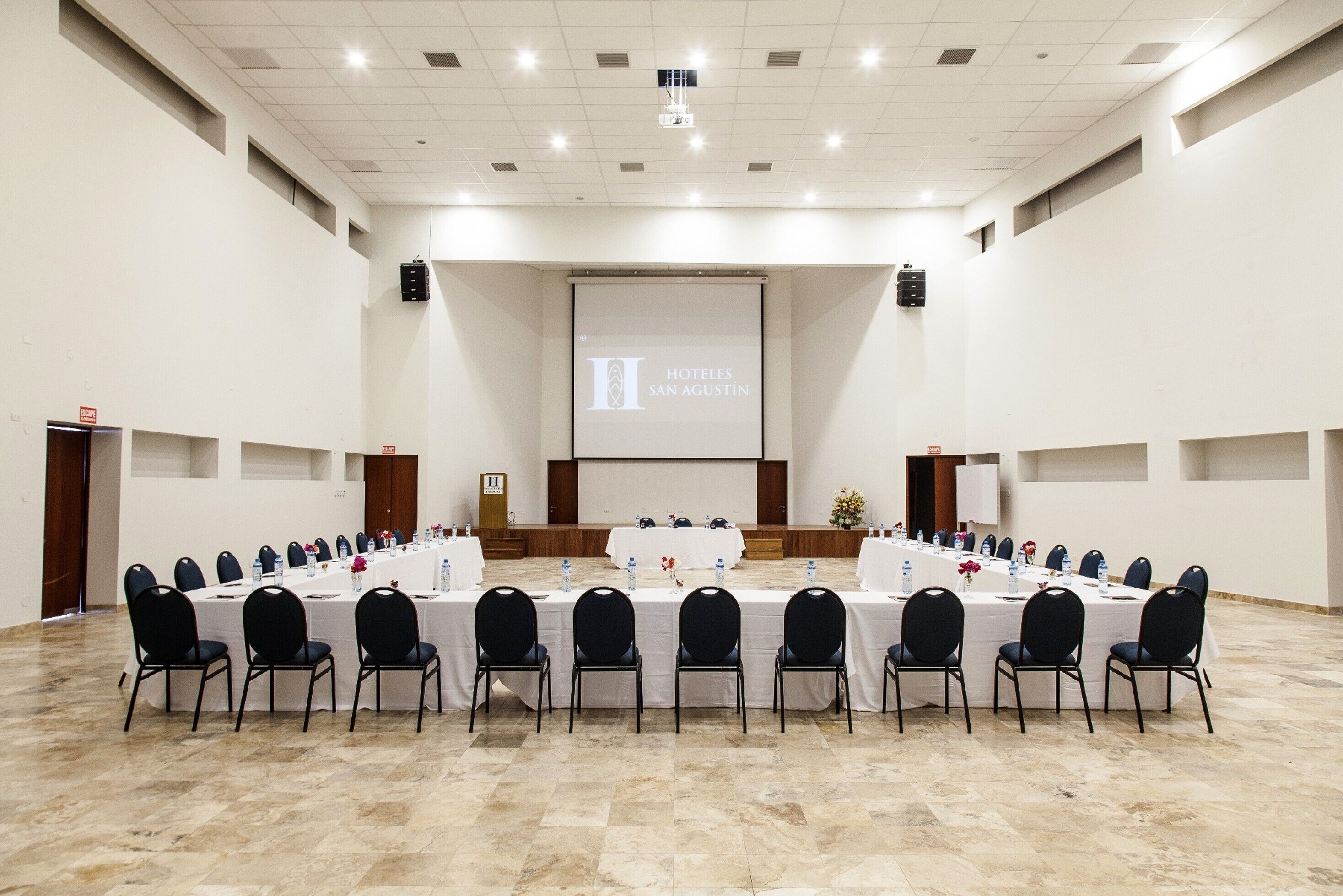 Un salón de conferencias con una larga mesa dispuesta para reuniones, equipado con sillas y botellas de agua.