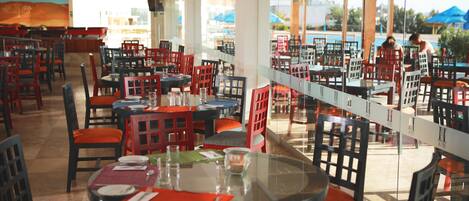 A restaurant with multiple tables and chairs, large windows, and a view of the outside.