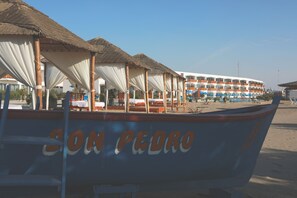 Un bateau nommé « SON PEDRO » a accosté sur une plage, avec un bâtiment visible au loin.