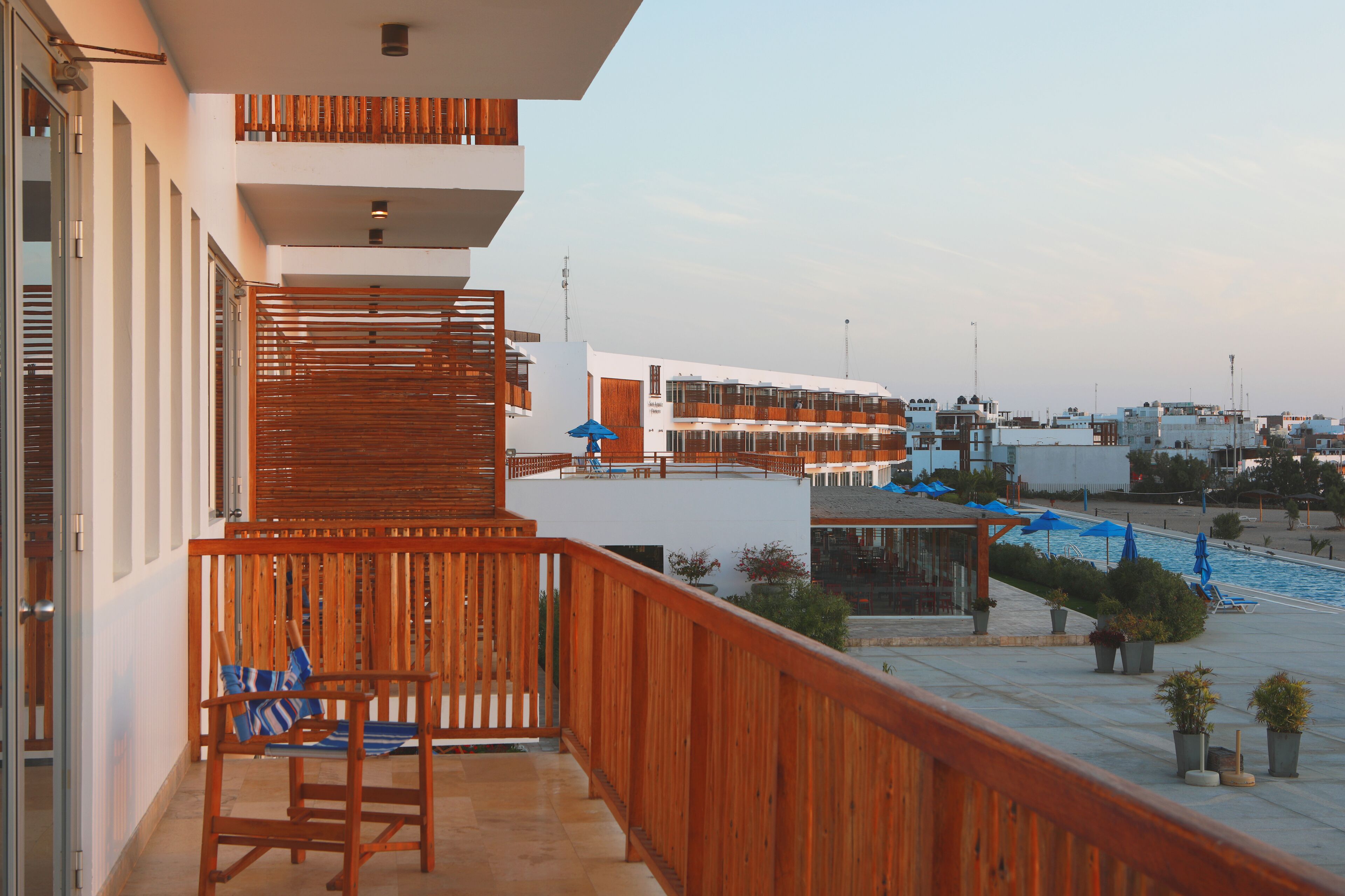 Ein Balkon mit Holzbalkonen, ein Poolbereich mit blauen Sonnenschirmen und Blick auf die umliegenden Gebäude.