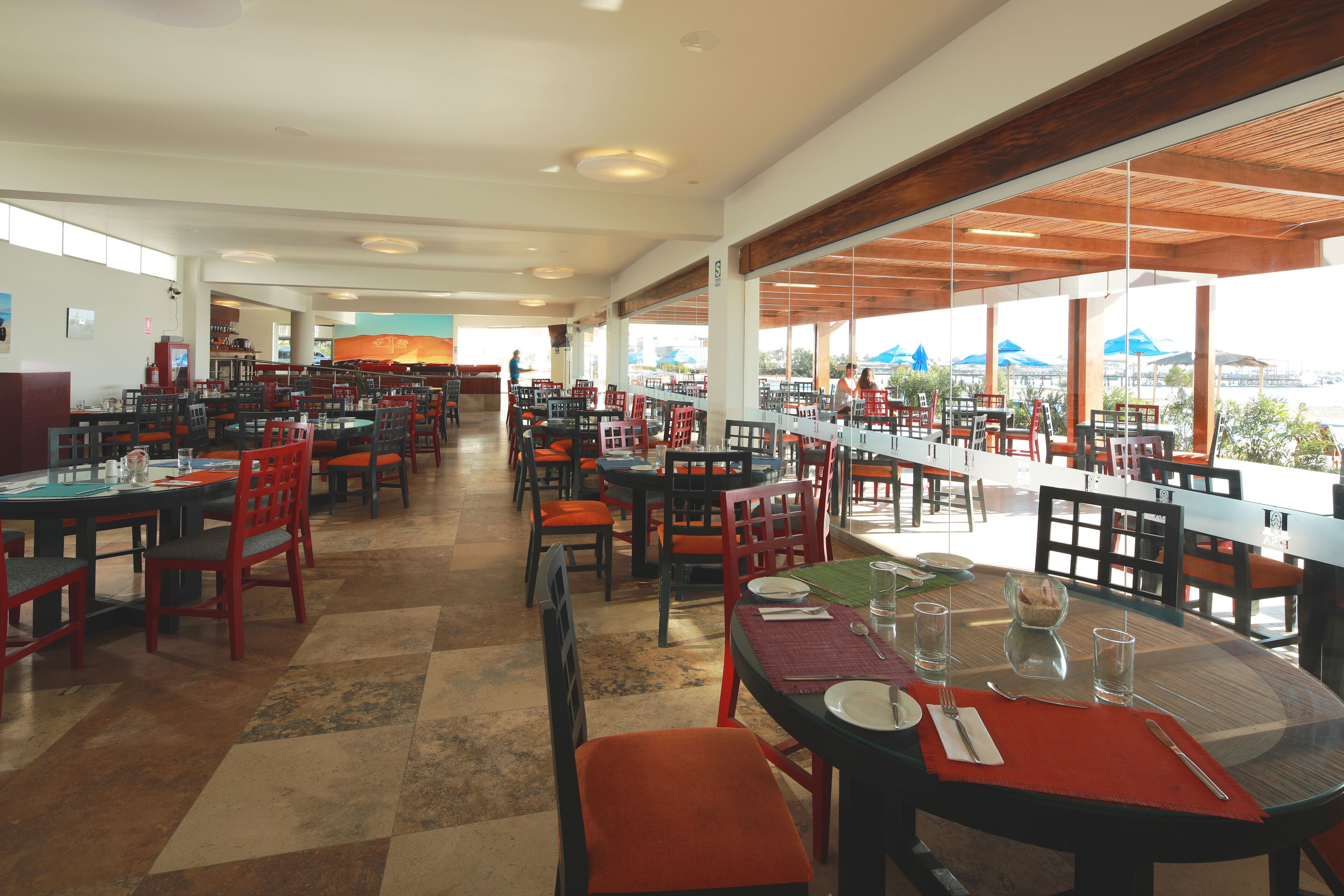 A spacious dining area with multiple tables and chairs, large windows offering views of the outdoors, and a clean, modern interior design.