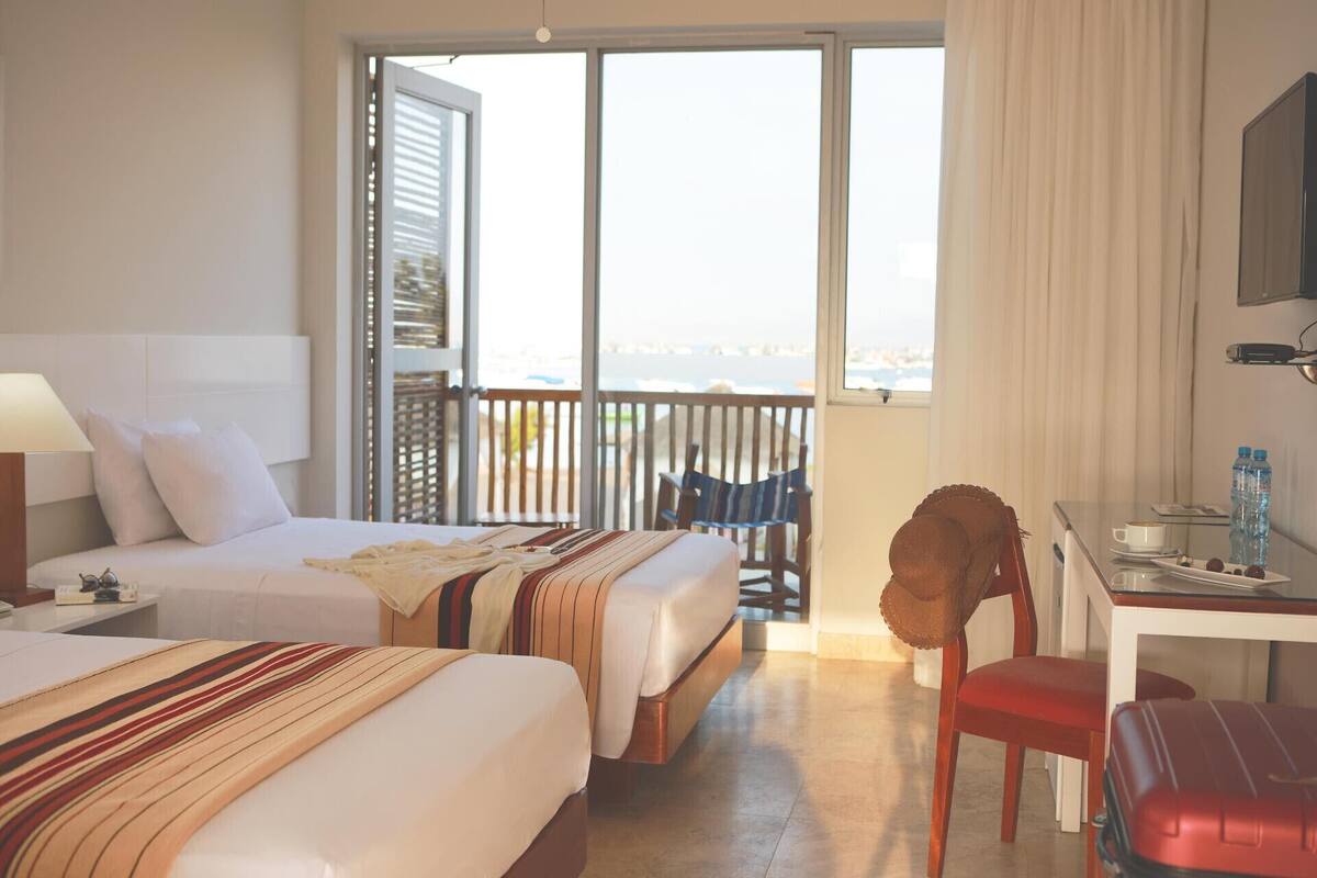 A hotel room with two beds, a desk, a chair, a television, and a balcony with a view.