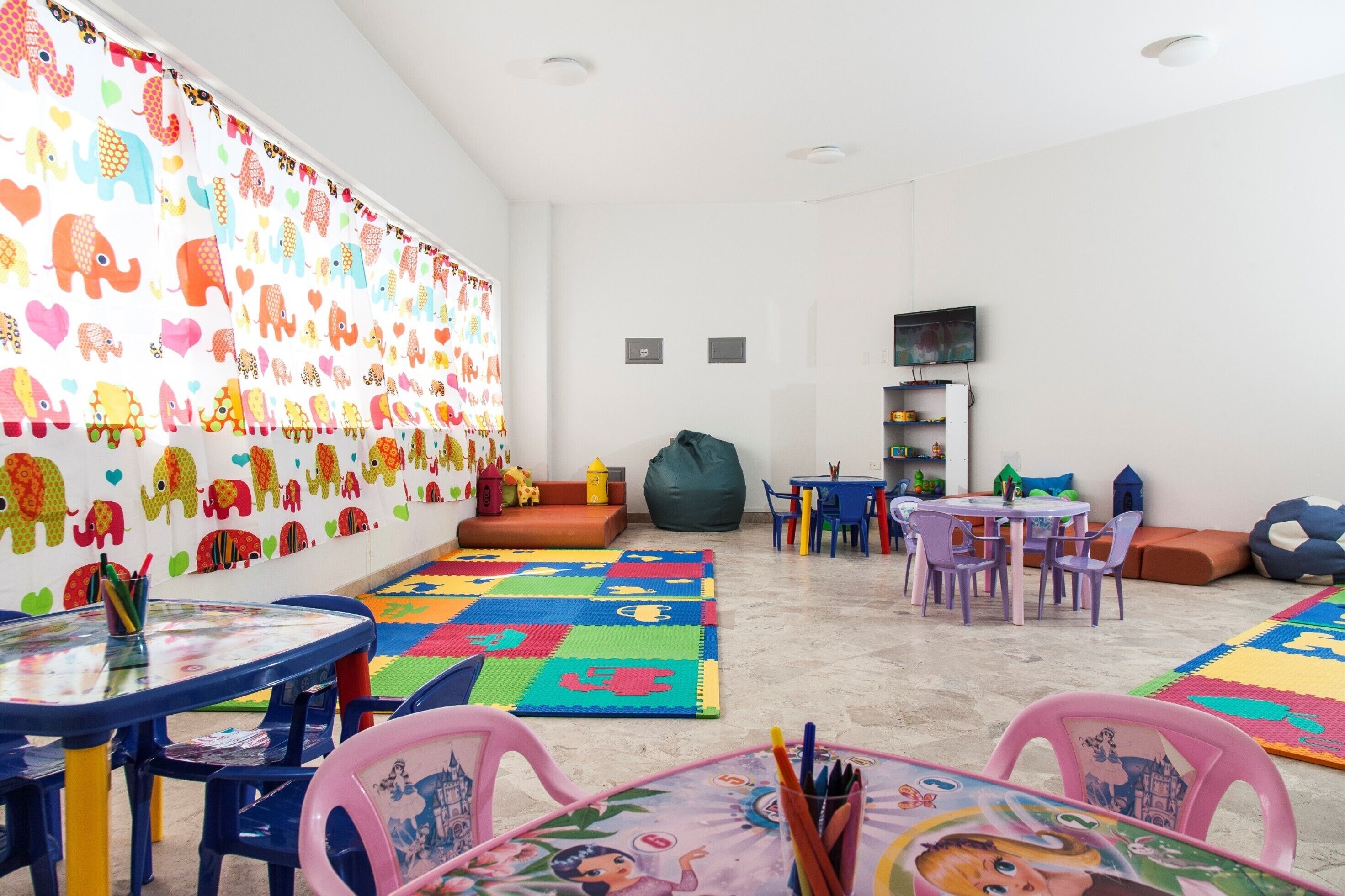 A children's playroom with colorful elephant wall decals, a play mat, and various toys.