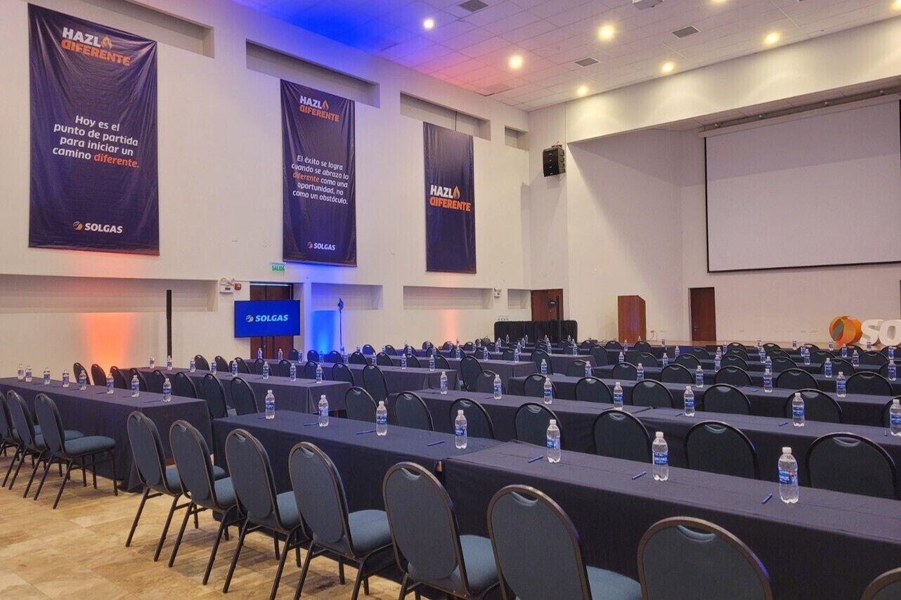 A conference room with rows of tables and chairs, banners with text, and a projection screen.