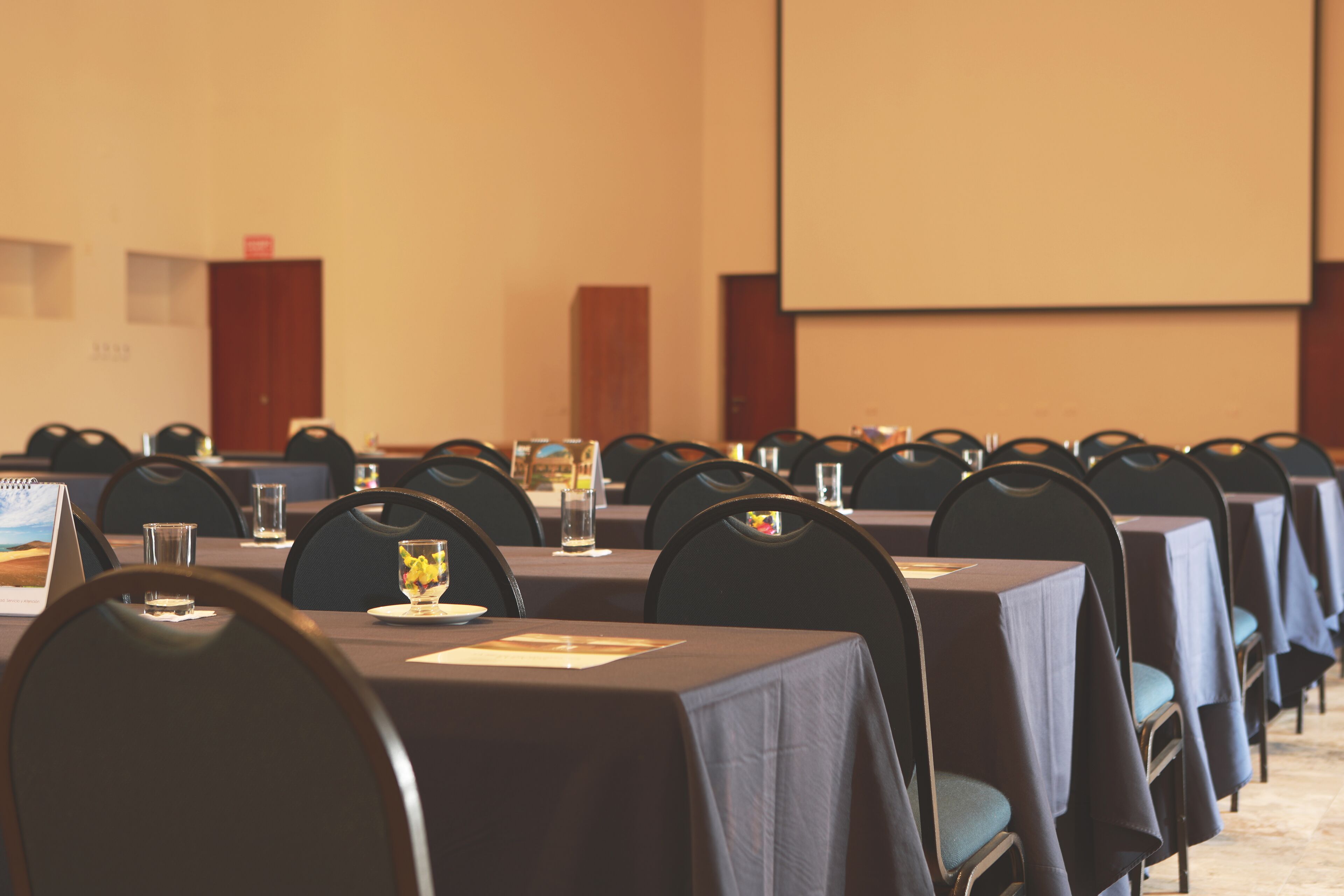 A conference room with rows of tables and chairs, a projector screen, and a podium.