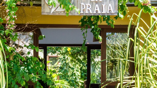 A wooden sign reading "BOSQUE DA PRAIA" above a covered entrance with lush greenery and a stone pathway. - Bosque da Praia - ePipa Hotéis (Tibau do Sul)