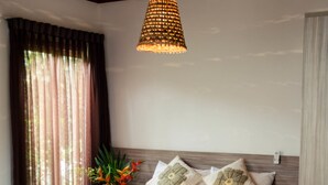 A neatly made bed with a patterned bedspread, a bedside table, and a hanging light fixture. - Bosque da Praia - ePipa Hotéis (Tibau do Sul)