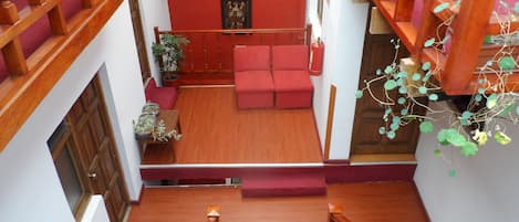 A multi-level interior with a staircase, red walls, a red sofa, wooden railings, and potted plants.