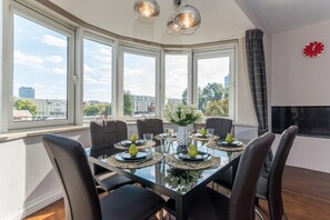 A modern dining area with a glass table, black chairs, and a city view through large windows. - P&O Apartments Center (Warsaw)
