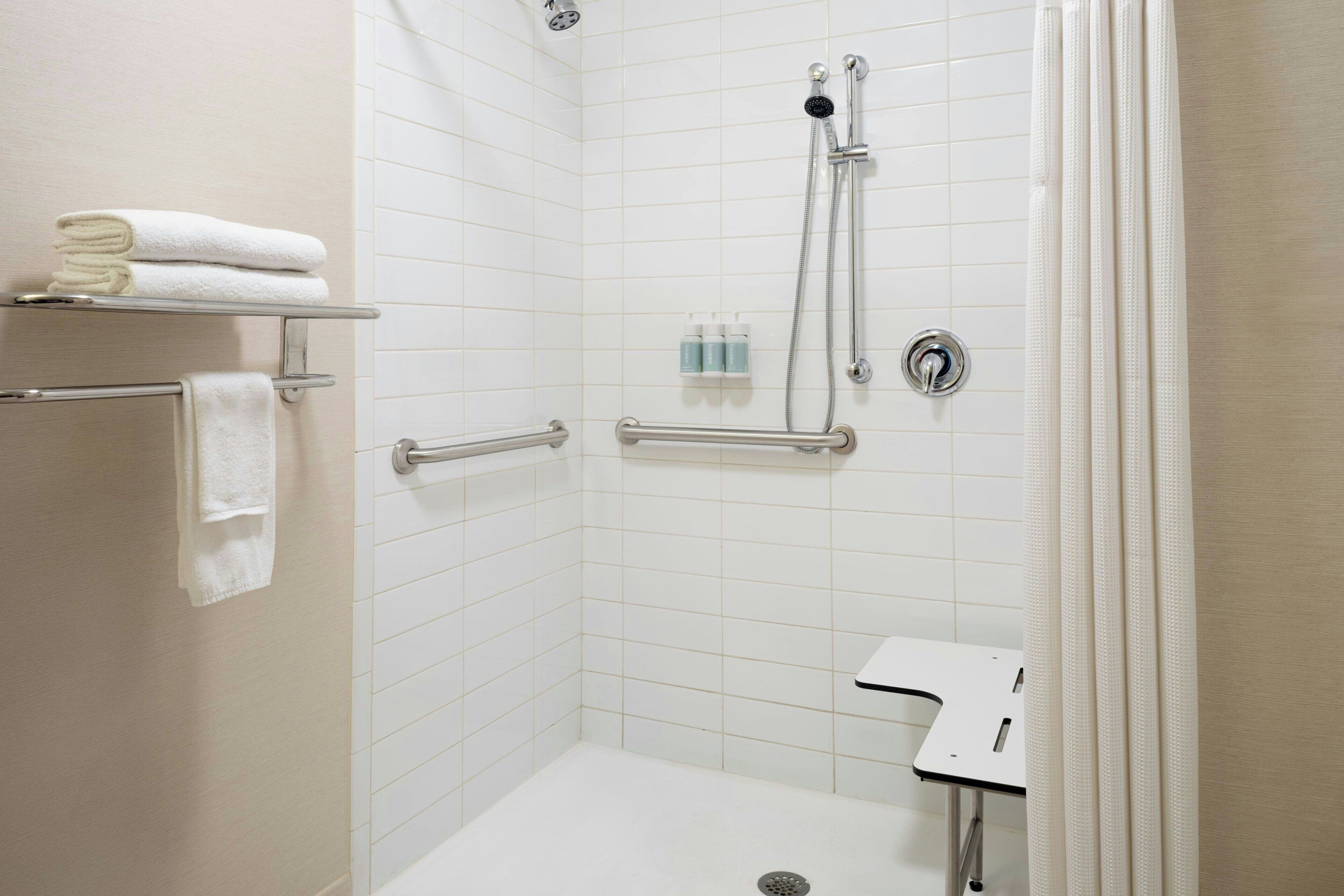 Ducha a nivel con paredes de azulejos blancos, cabezal de ducha manual y barra de apoyo.